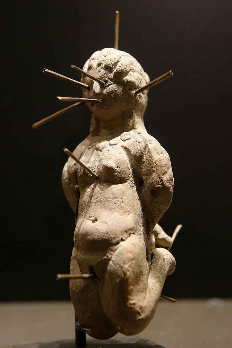 A voodoo doll with bound arms and needles, via Wikimedia