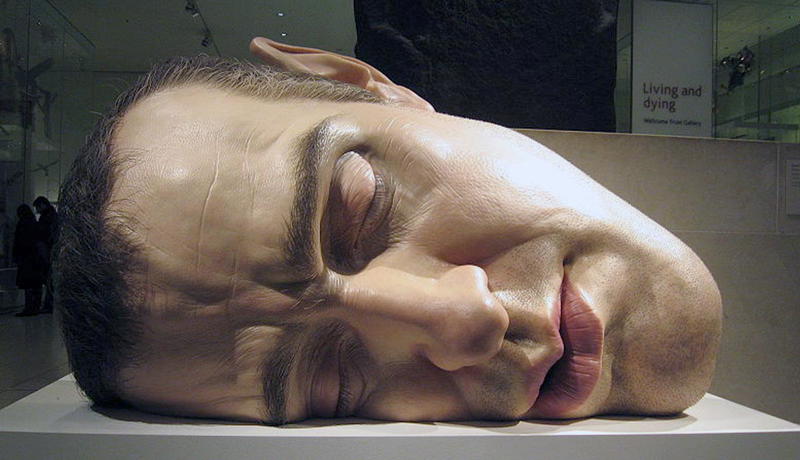 Hyperrealistic oversized sculpture of a man’s head lying on its side