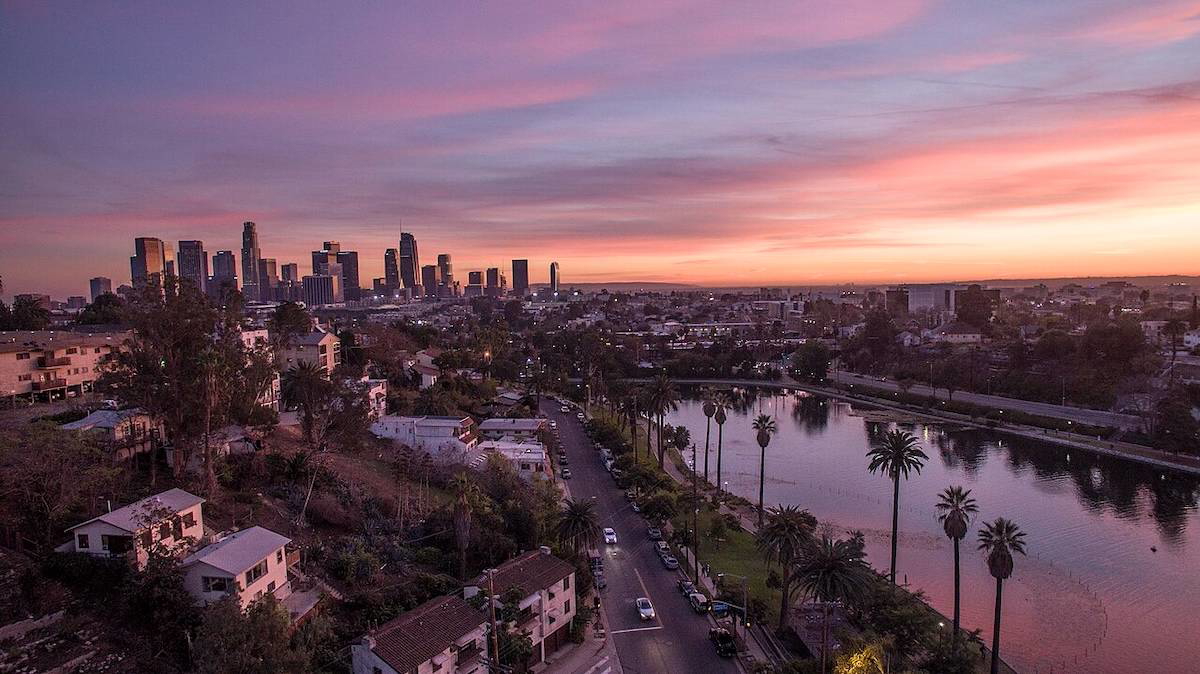 View of Downtown Los Angeles skyline with Echo Park Lake in the foreground under a partly cloudy sky.