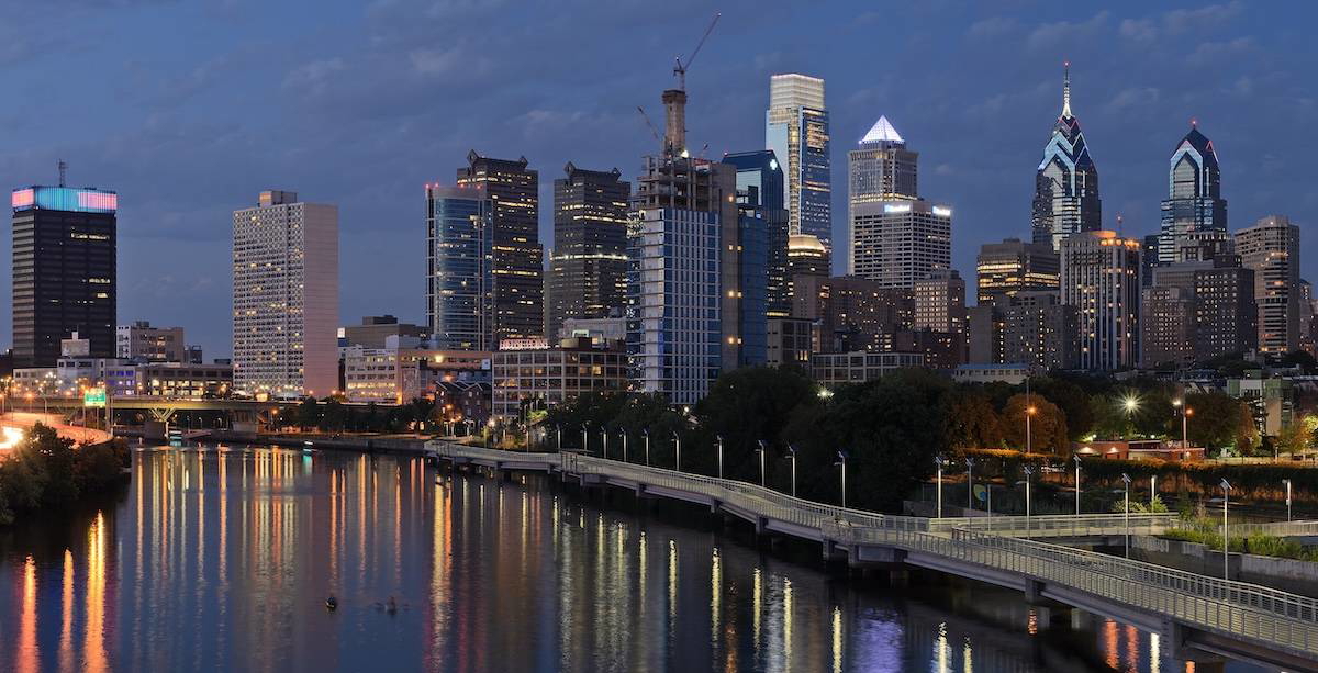 Panoramic view of Philadelphia from South Street Bridge showing skyline, buildings, and urban streets under a clear sky.