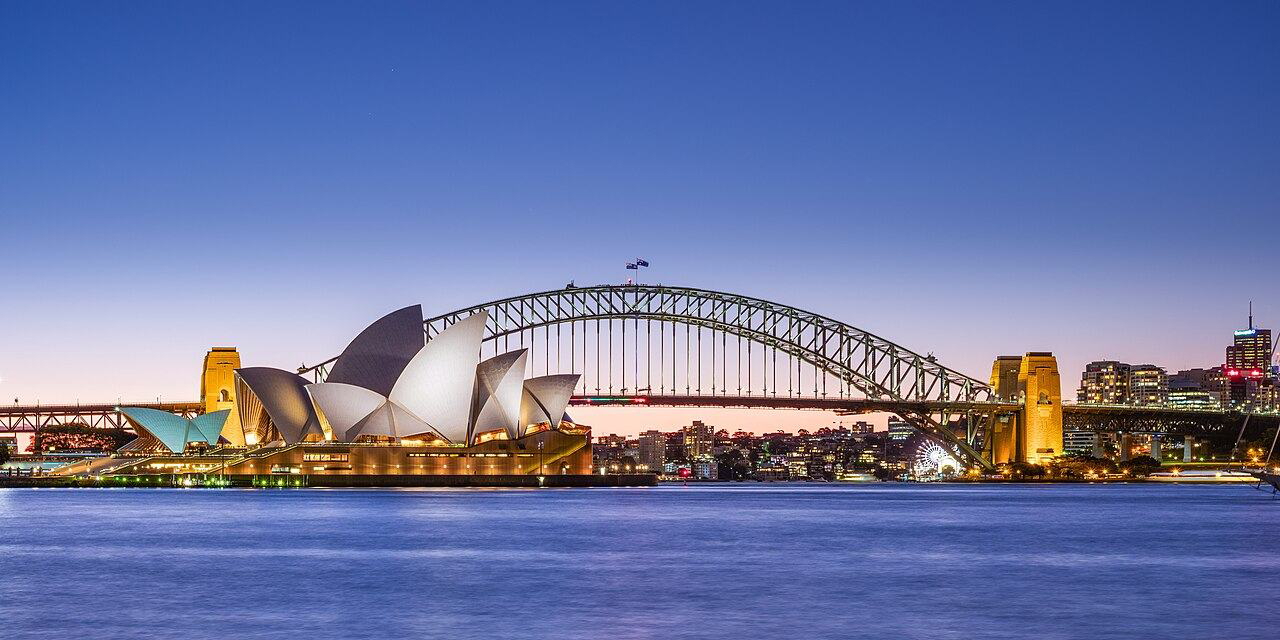 Sydney Opera House and Harbour Bridge at dusk with colorful reflections on the water.