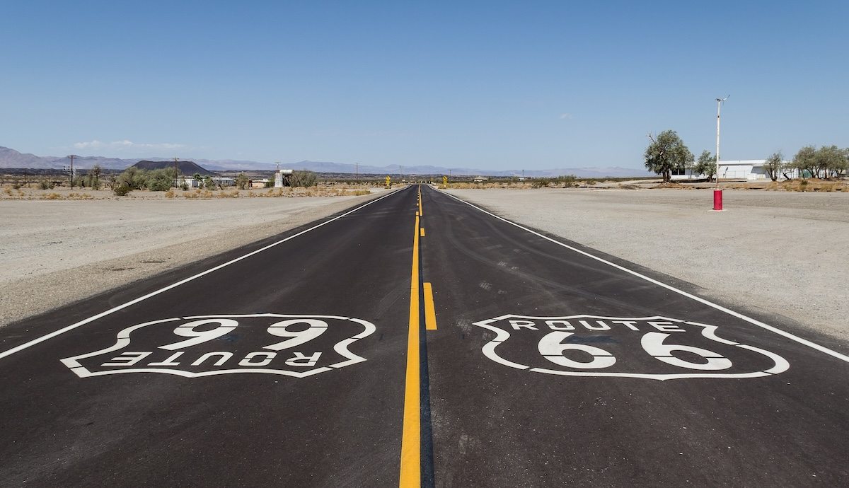 Wide view of historic Route 66 passing through Amboy, California, with Roy’s Motel and Café visible against the Mojave Desert backdrop