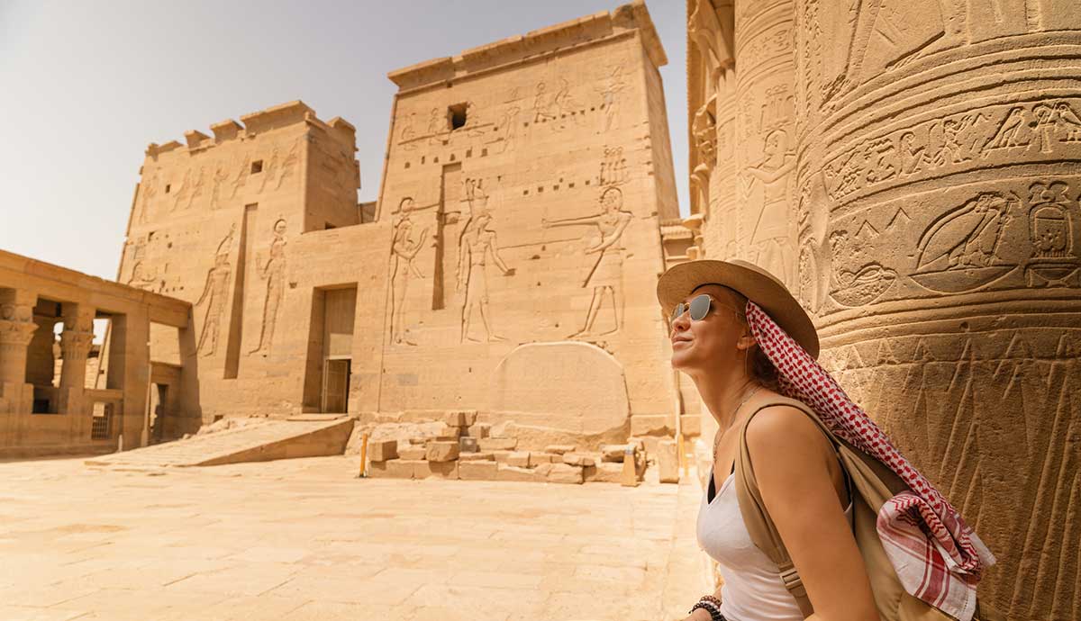 Temple of Isis (or Temple of Philae) in the ancient city of Aswan, Egypt, with a woman sitting admiring the walls.