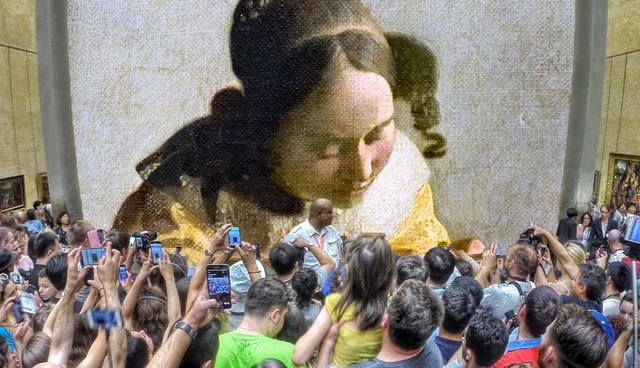 Crowd photographing a large mosaic portrait in a museum.